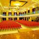 A wedding hall with hundreds of red coloured chairs arranged for guest seating, ceiling lights and decor beautify the hall.