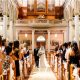 A Christian bride with her father walking into the church for her wedding and guests looking at her.