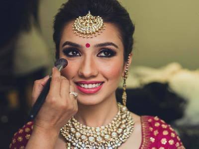 A smiling bride getting her make up done for wedding, adorning kundan jewelry