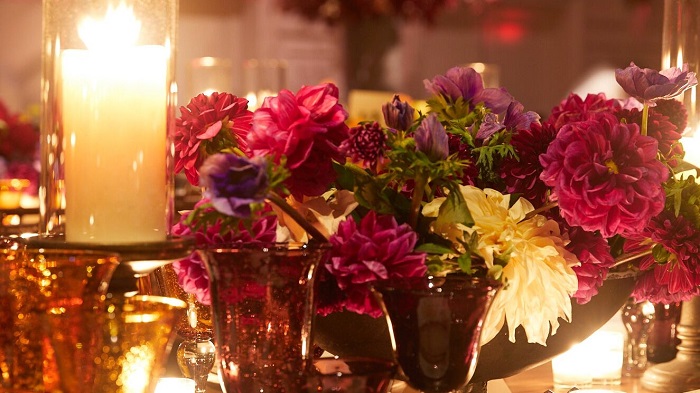 Colorful flowers arranged in the small flower vases, a candle can be seen closeby.